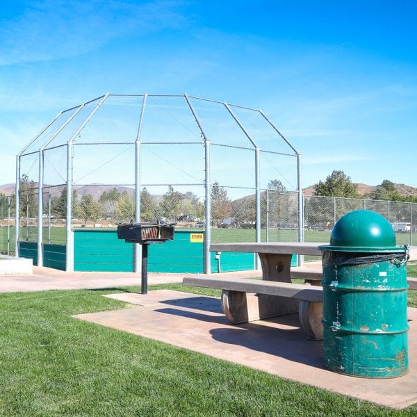Picnic table, BBQ grill and trash can behind a baseball net